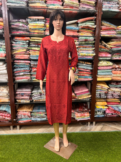lucknowi chikankari A red long-sleeve kurta displayed on a female mannequin, standing in front of shelves filled with folded colorful fabrics.