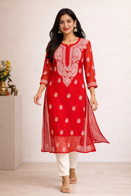A woman modeling a red kurta set with white embroidery, paired with white pants, in a clean indoor setting.