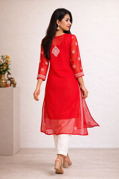 A woman modeling a bright red three-quarter sleeve kurta with white embroidered details, paired with white pants and beige heels, shown from a rear three-quarter view against a neutral indoor background.