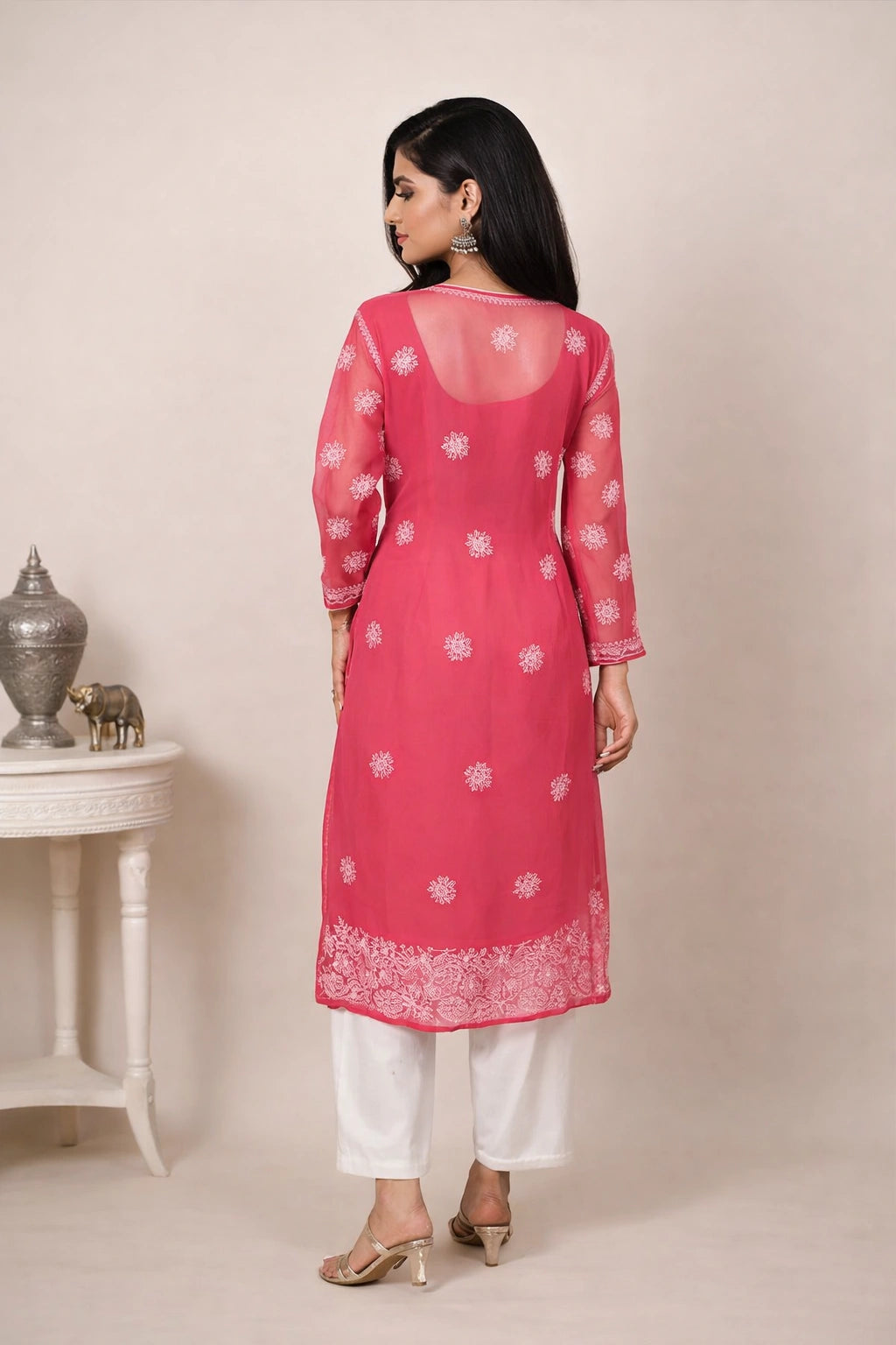 Woman wearing a pink kurta with white patterns and white pants, standing against a plain background.