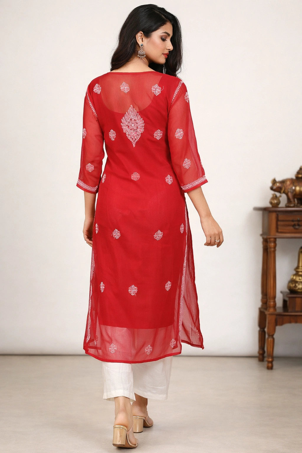Woman wearing a red embroidered kurta with white pants against a plain background