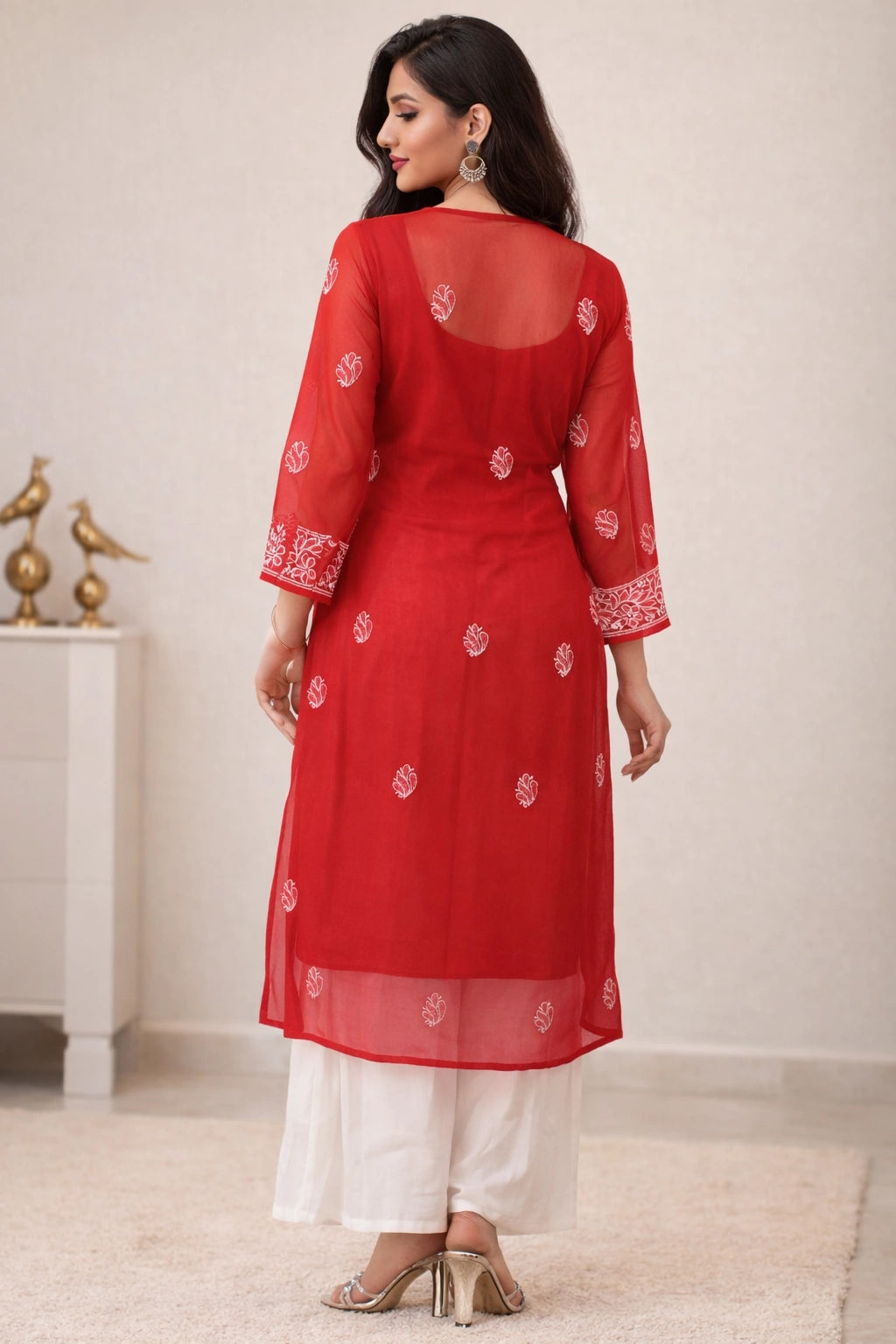 Woman wearing a red embroidered kurta with white pants in a minimal indoor setting.