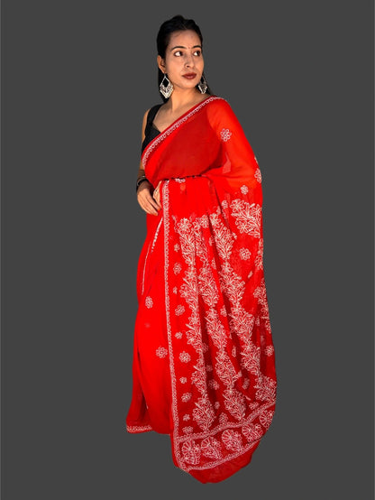 A woman modeling a bright red saree with intricate white floral embroidery and a black sleeveless blouse, set against a solid dark gray background.