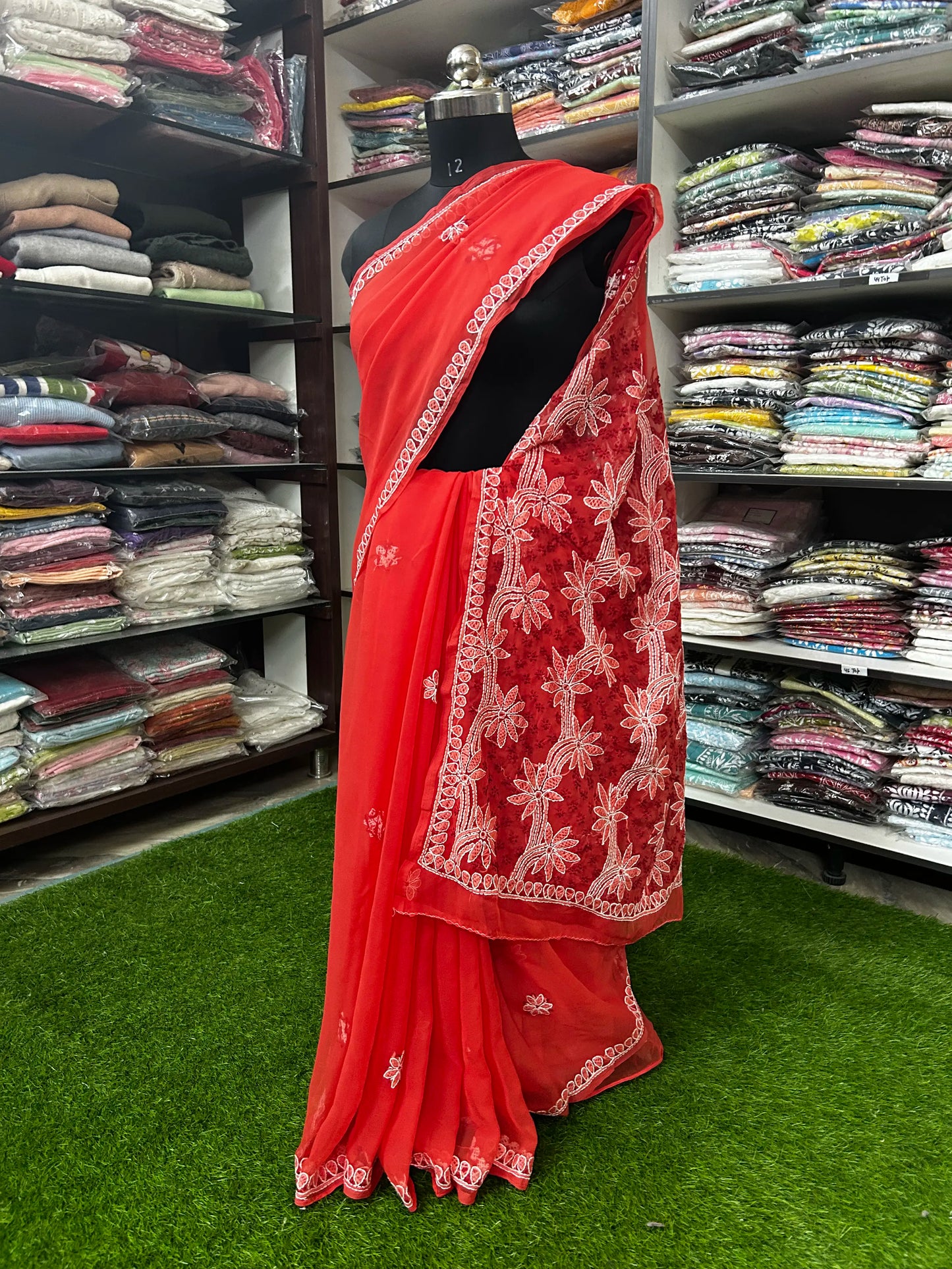 Red saree with white embroidery on a mannequin in a clothing store.