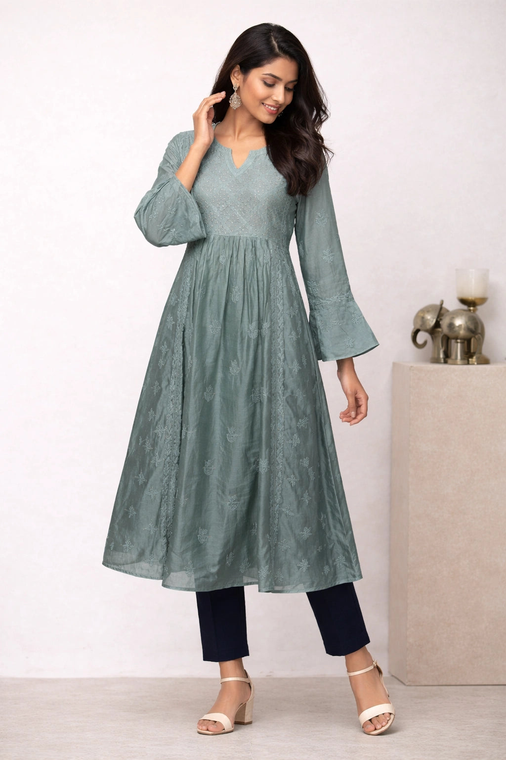 Woman wearing a green dress with long sleeves and black pants on a white background