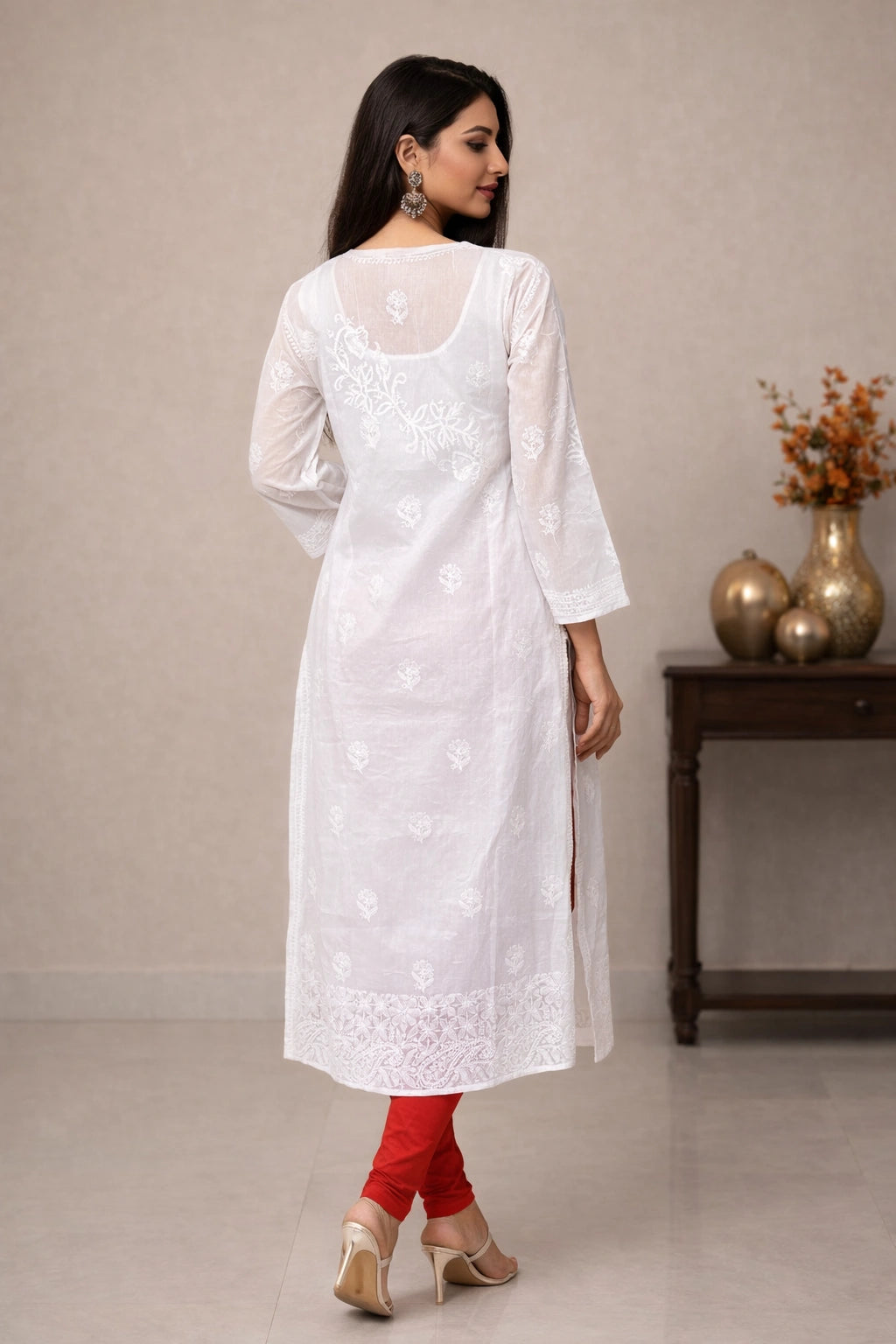 Woman wearing a white embroidered kurta with red pants in a minimalistic setting.