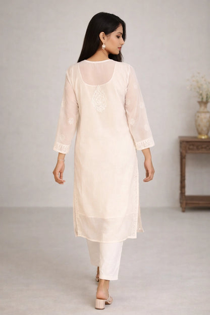 Lucknowi chikankari A woman wearing a light cream/off-white kurta with white pants, shown from the back in a studio setting with a neutral background and a side table.