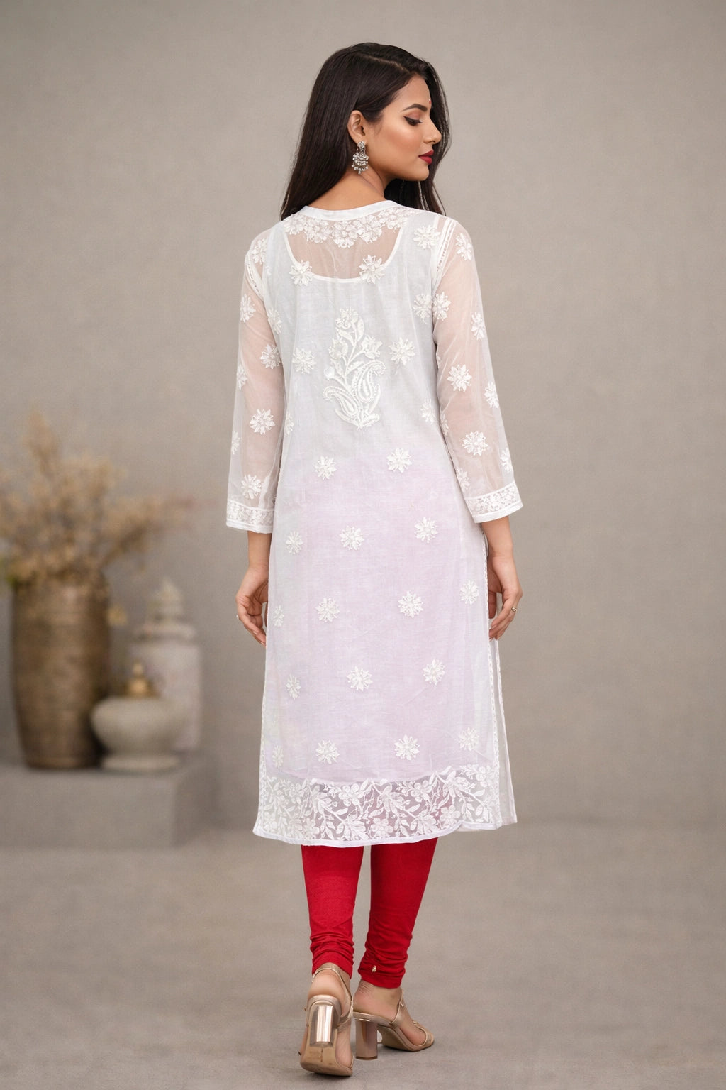 Woman wearing a white embroidered kurta with red pants against a neutral background