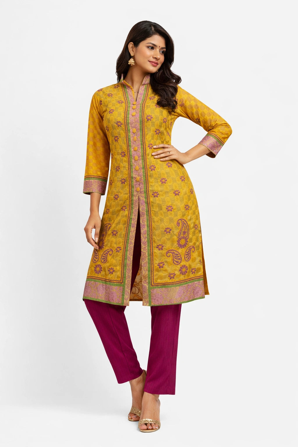 Lucknowi chikankari A woman modeling a mustard yellow kurta with pink and purple floral patterns and magenta pants against a light gray studio background.