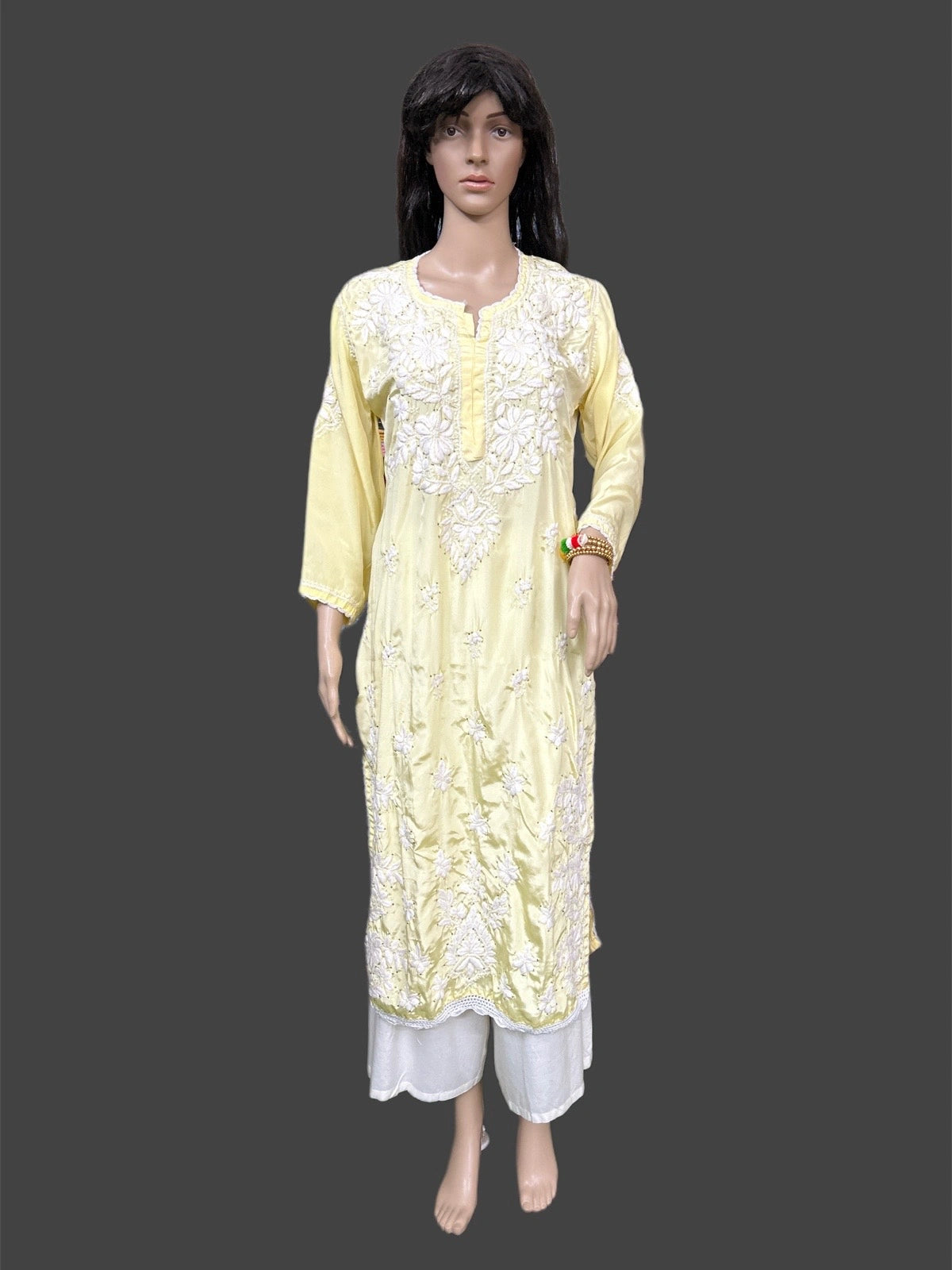 Mannequin wearing a light yellow embroidered kurta with white pants on a dark background