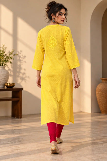 A woman wearing a bright yellow embroidered kurta with three-quarter sleeves and red leggings, shown from the back in a warm, sunlit indoor setting.