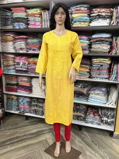 A yellow embroidered kurta displayed on a female mannequin, paired with red leggings, set against a background of shelves filled with folded colorful garments.
