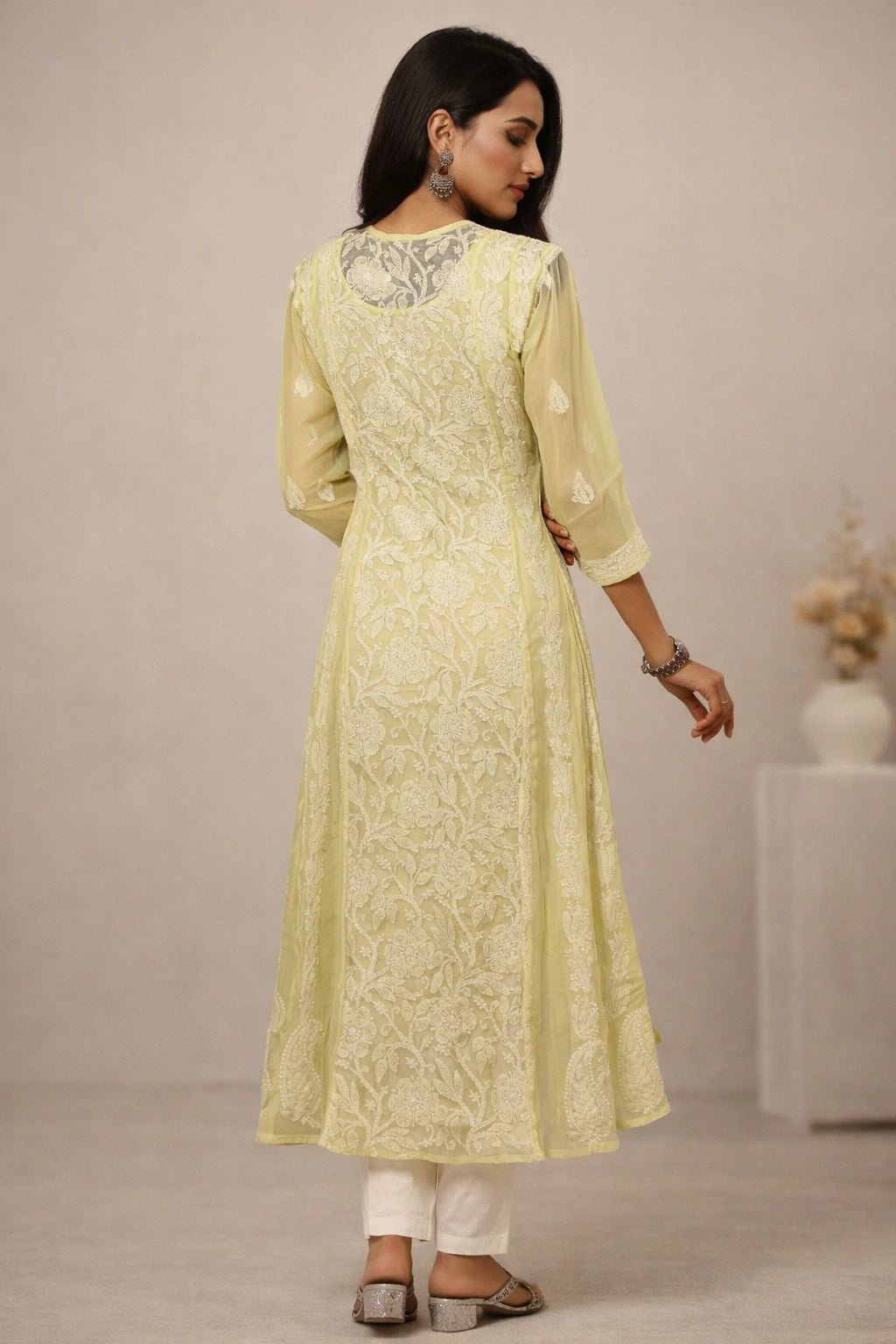 Woman wearing a light yellow embroidered kurta with white pants against a neutral background