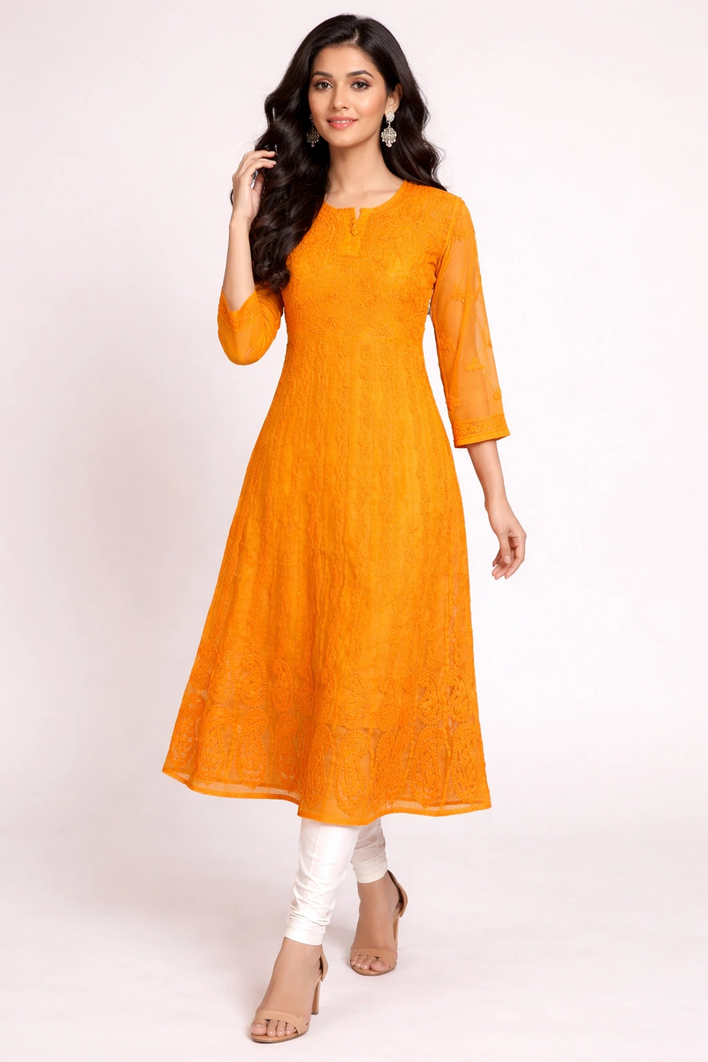 Woman wearing an orange lucknowi chikankari kurta with white pants on a light pink background