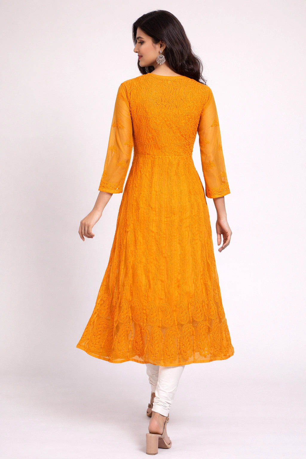 Woman wearing a bright orange lucknowi kurta with white pants on a white background