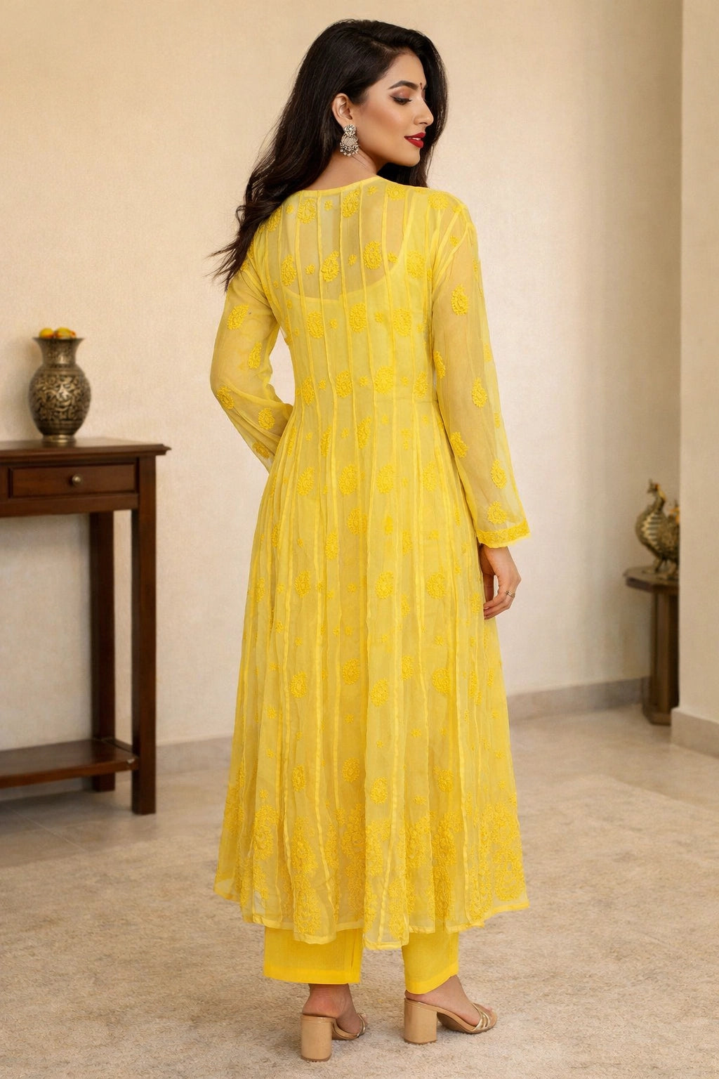 Woman wearing a yellow dress standing in a room with a wooden table and decorative items.