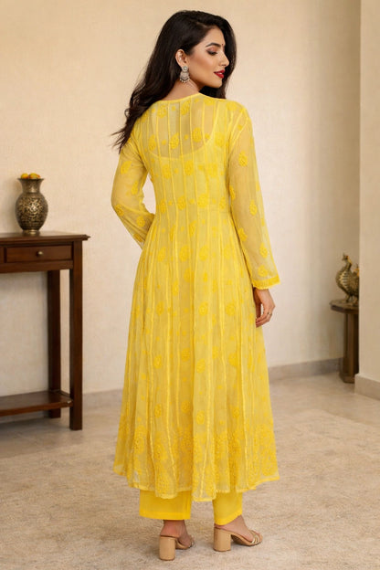 Woman wearing a yellow dress standing in a room with a wooden table and decorative items.