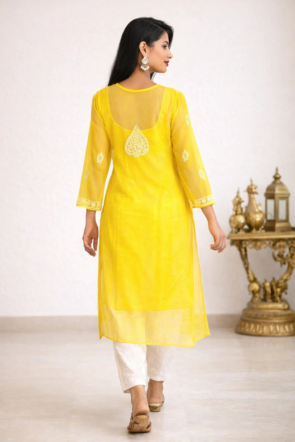 Lucknowi chikankari A woman modeling a bright yellow kurta with white pants in an indoor setting with a decorative gold table in the background.
