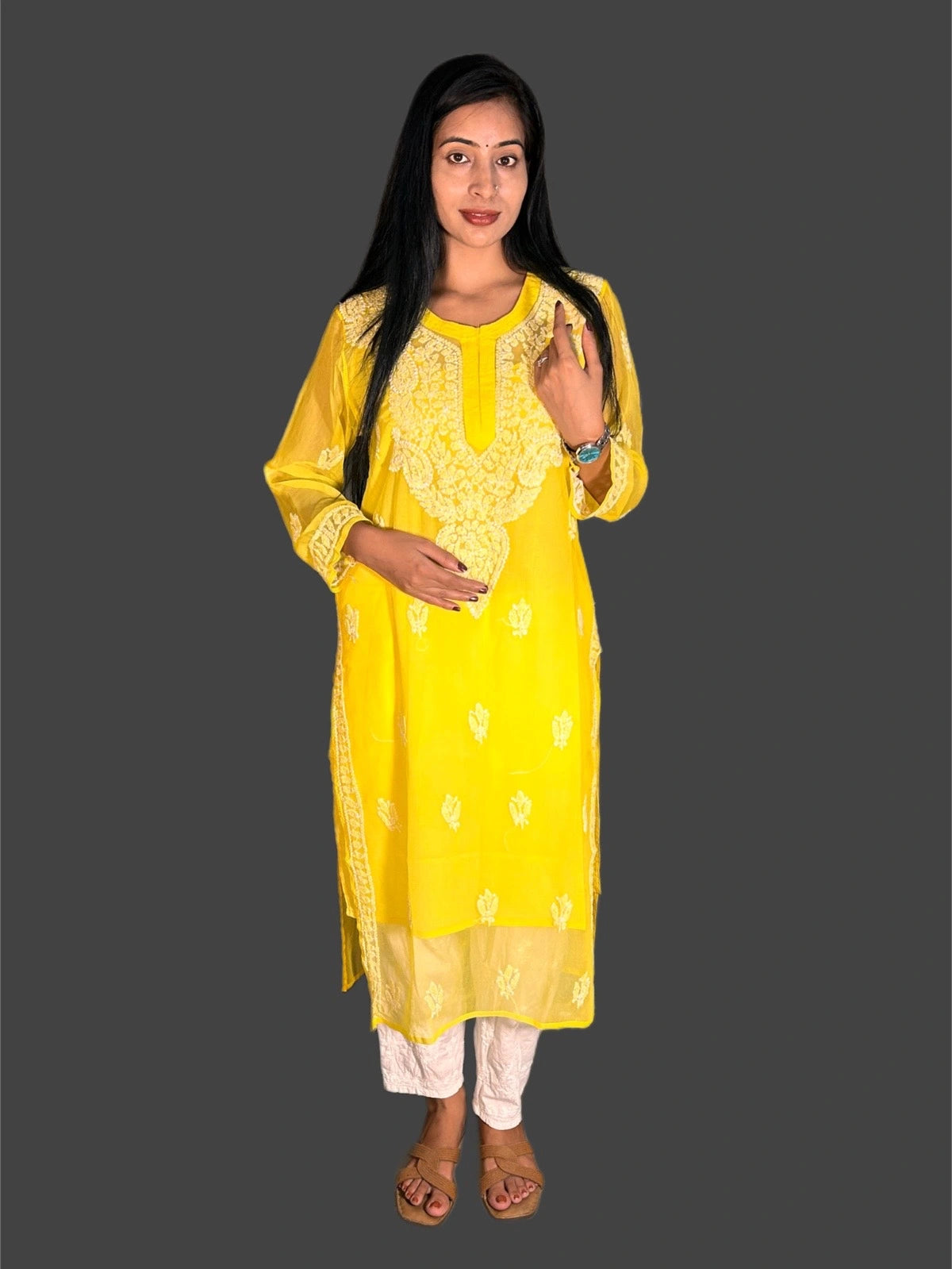 A woman modeling a bright yellow embroidered kurta with white pants, standing against a solid dark gray background.