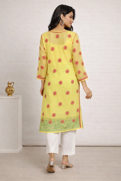 Woman wearing a lucknowi yellow kurta with red floral patterns and white pants against a plain background