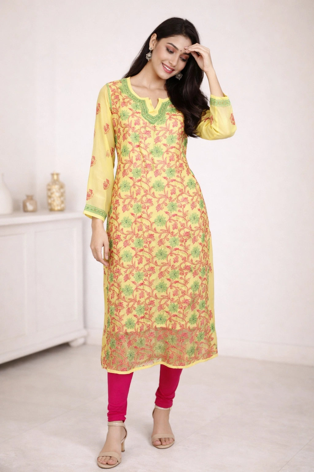 Woman wearing a yellow and green floral kurta with pink pants in a minimalistic setting.