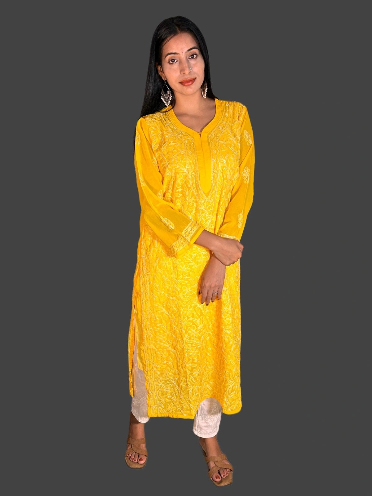 A woman modeling a bright yellow embroidered kurta with matching pants, standing against a solid dark gray background.