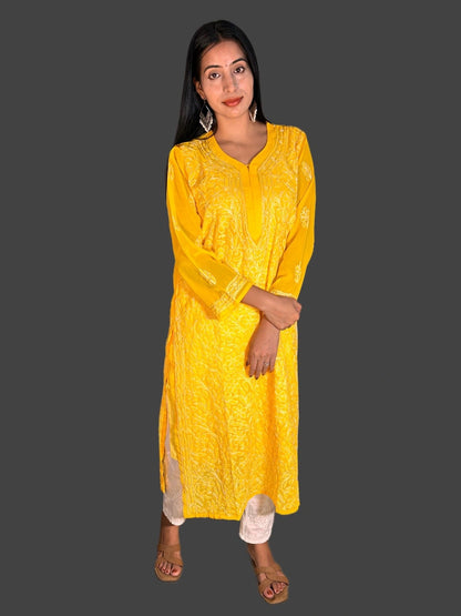 A woman modeling a bright yellow embroidered kurta with matching pants, standing against a solid dark gray background.