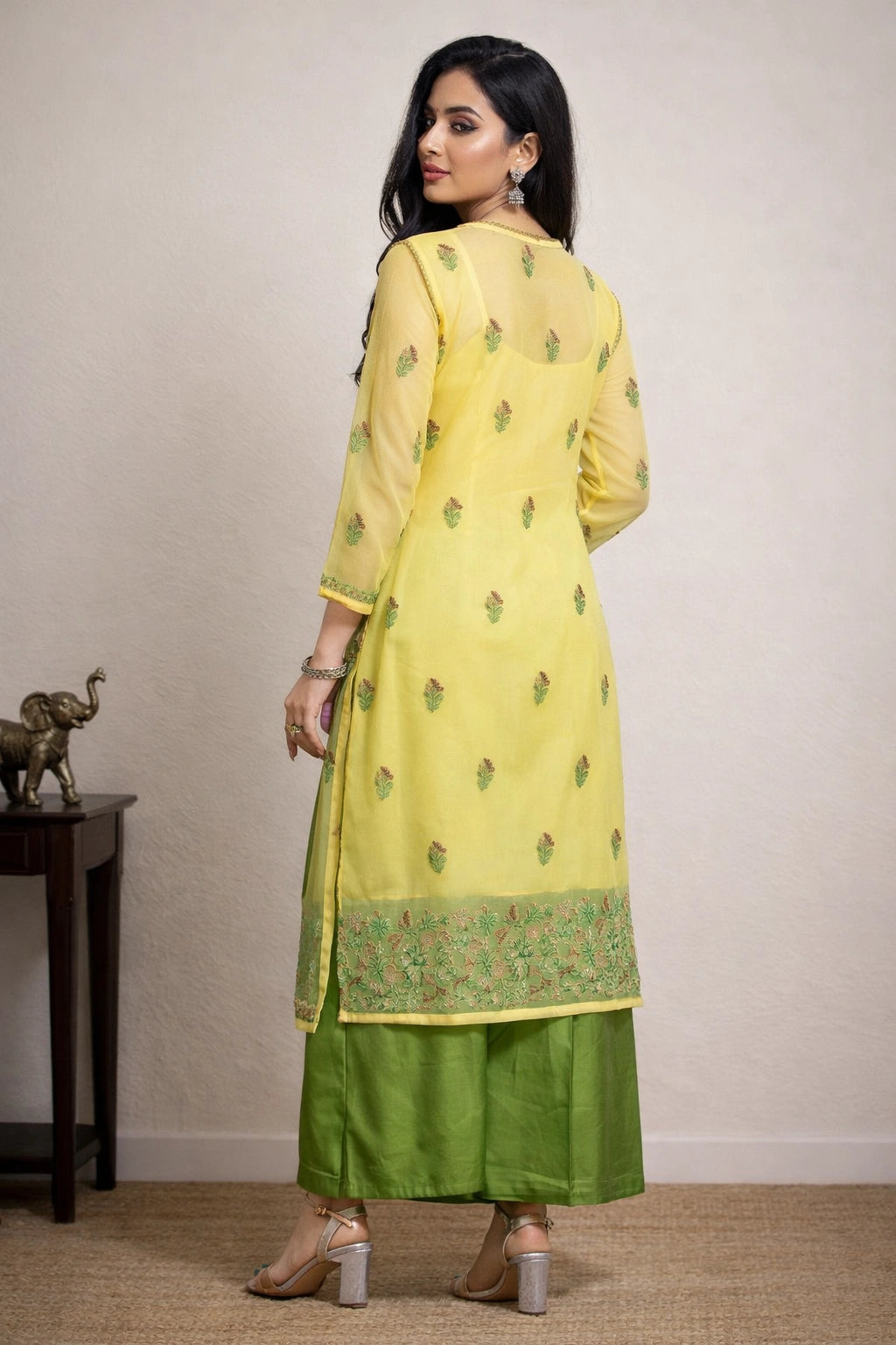 Woman wearing a yellow and green traditional outfit in a room with a plain background