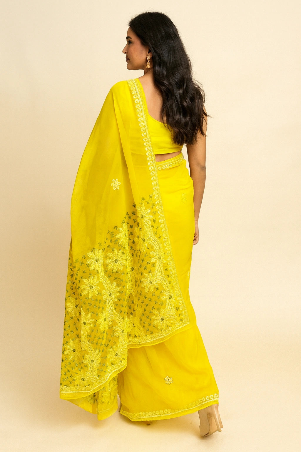 Woman wearing a lucknowi chikankari bright yellow saree with a matching blouse on a beige background