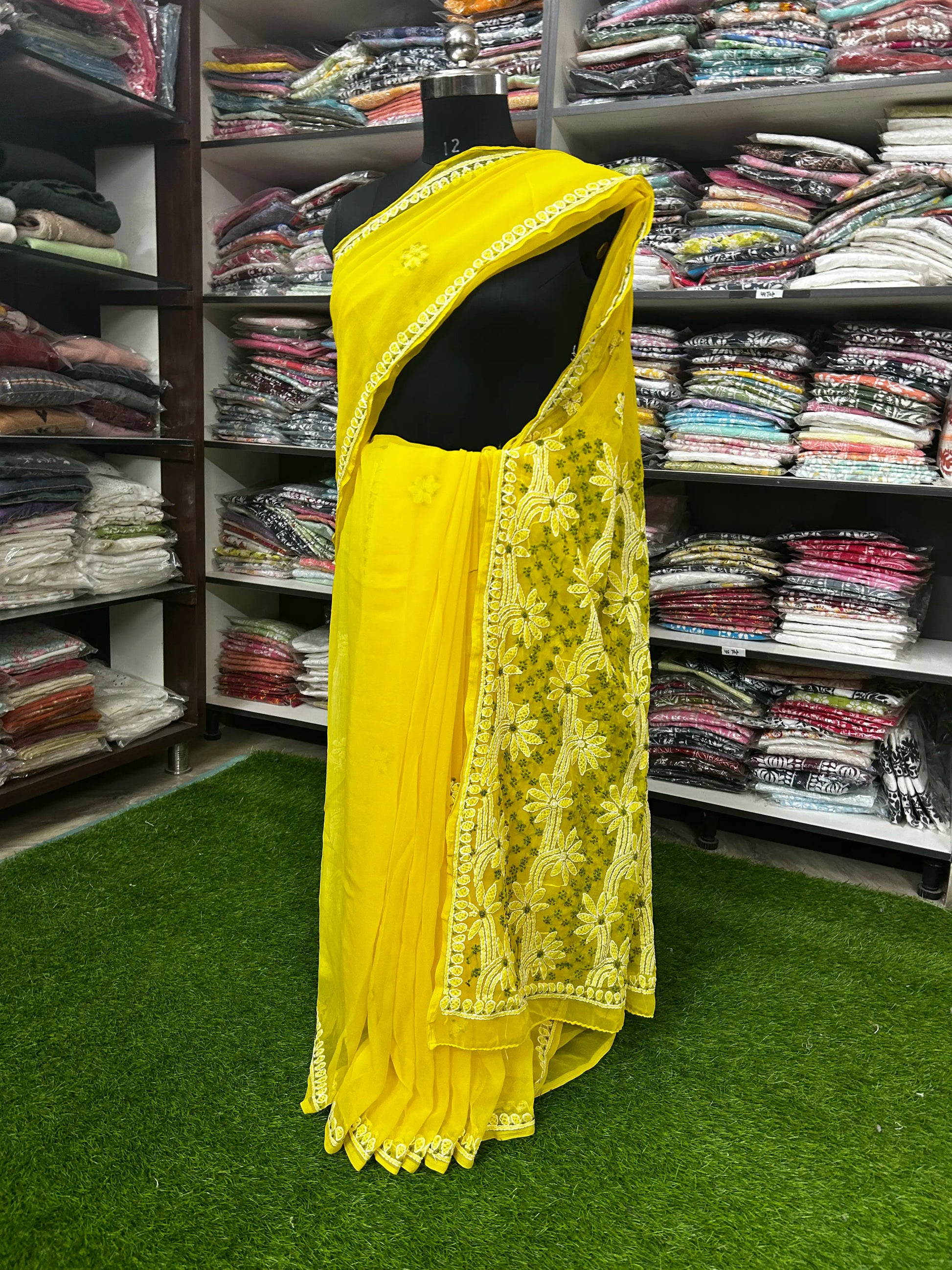 Lucknowi chikankari Yellow saree with lace details on a mannequin in a clothing store.