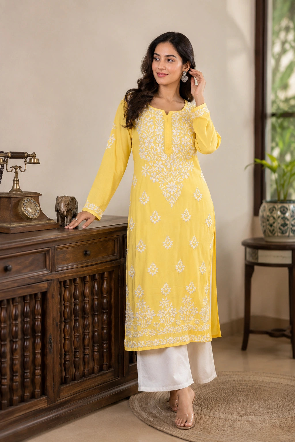 Woman in a yellow kurta with white patterns standing in a room with wooden furniture and decor.