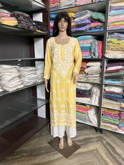 lucknowi chikankari Mannequin wearing a yellow and white dress in a fabric store with shelves of colorful fabrics.