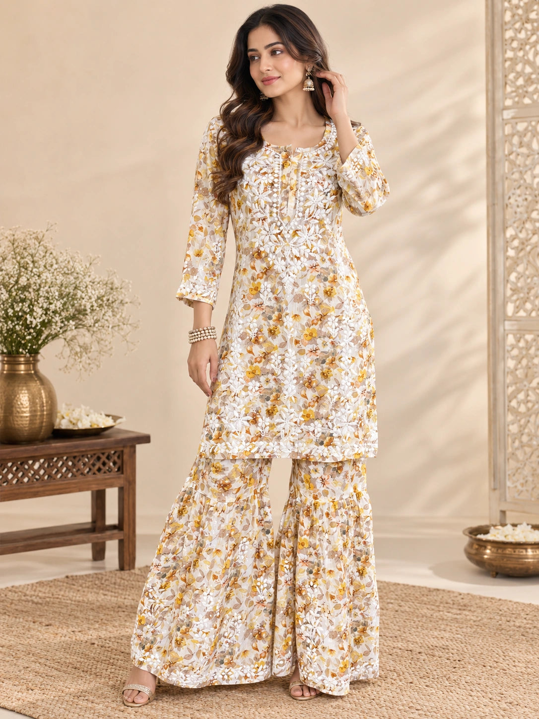 Lucknowi chikankari A woman models a three-piece white and yellow floral print kurta set in a warm, neutral-toned indoor setting with a wooden table and decorative vase.