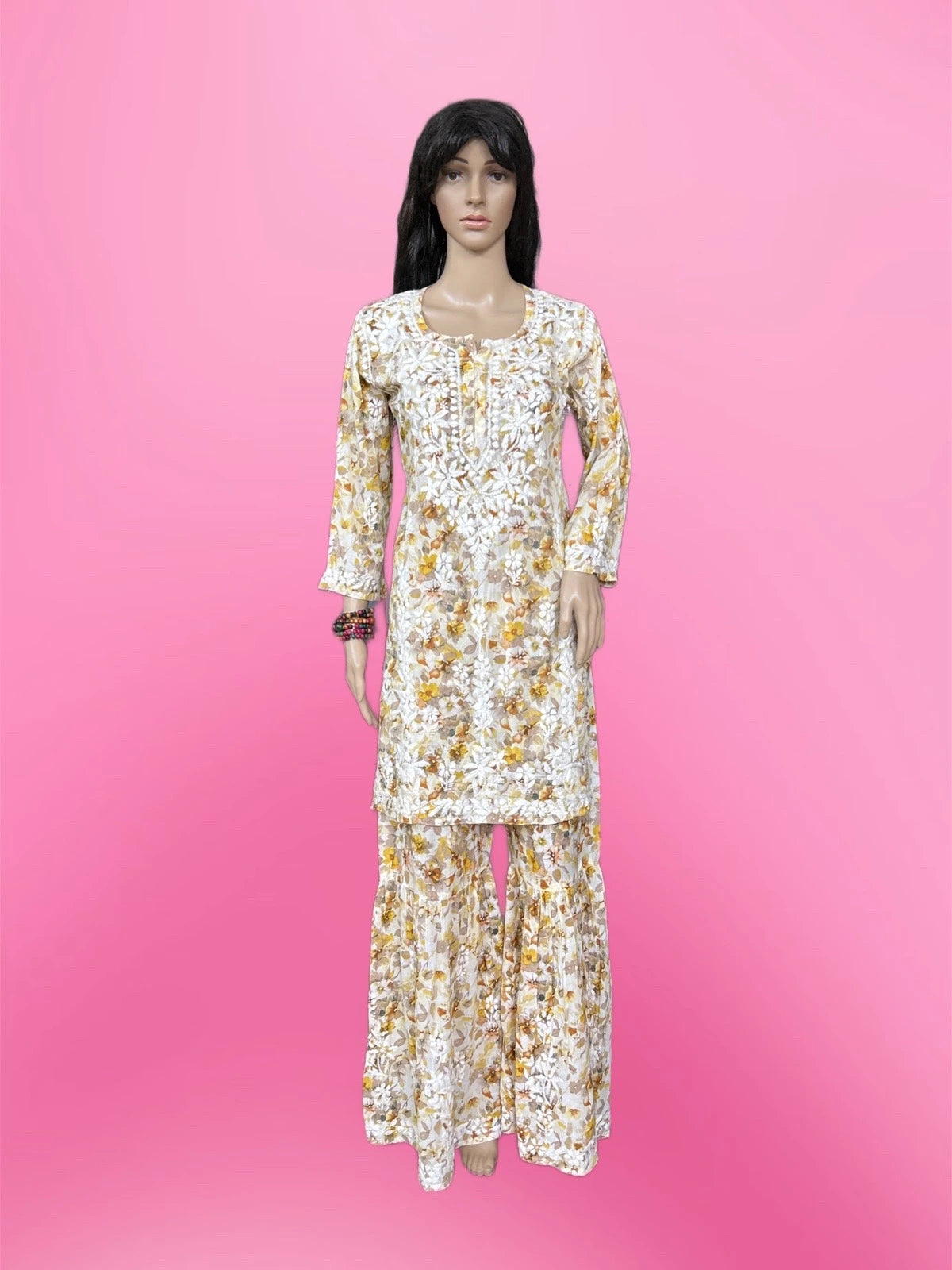 Lucknowi chikankari A mannequin wearing a long-sleeve kurta and matching wide-leg pants set with a white base and yellow floral pattern, set against a solid pink background.