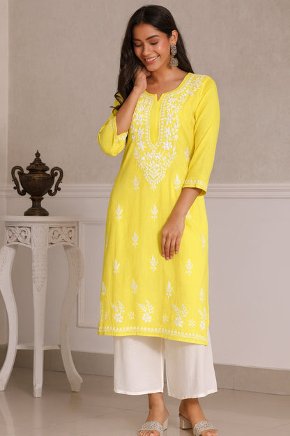 Woman wearing a yellow embroidered kurta with white pants in an indoor setting.