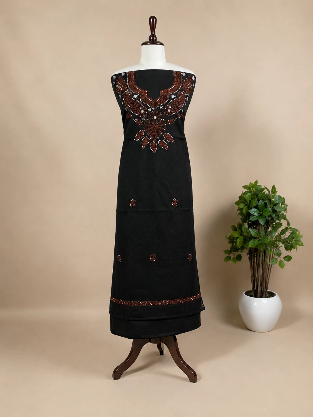 Black dress with intricate embroidery on a mannequin against a beige background