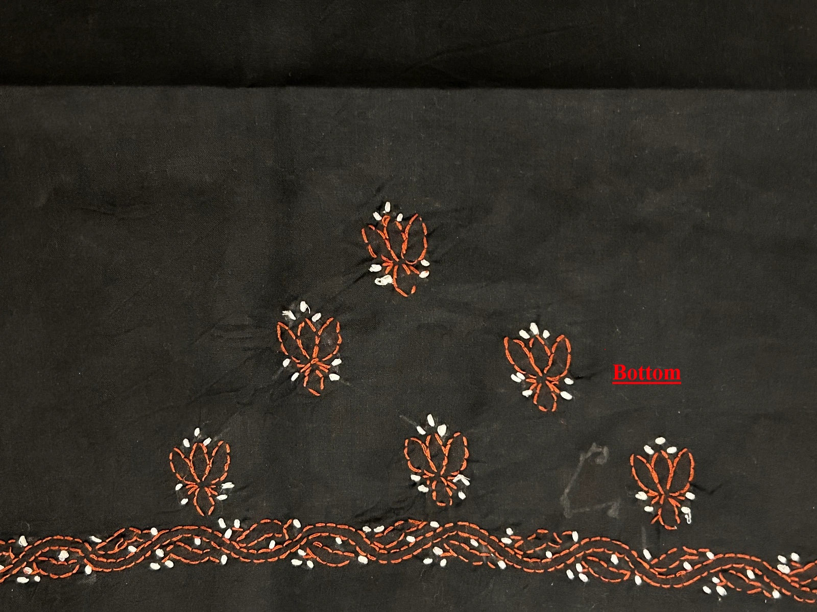 Black fabric with intricate brown and white embroidery on a dark background