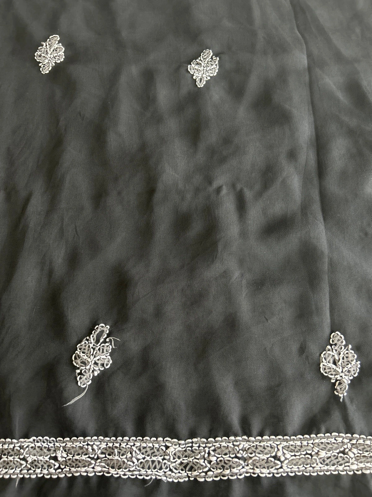 Close-up of a dark charcoal gray fabric with delicate silver metallic embroidery and a decorative embroidered border along the bottom edge.