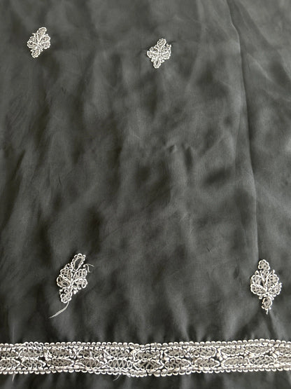 Close-up of a dark charcoal gray fabric with delicate silver metallic embroidery and a decorative embroidered border along the bottom edge.