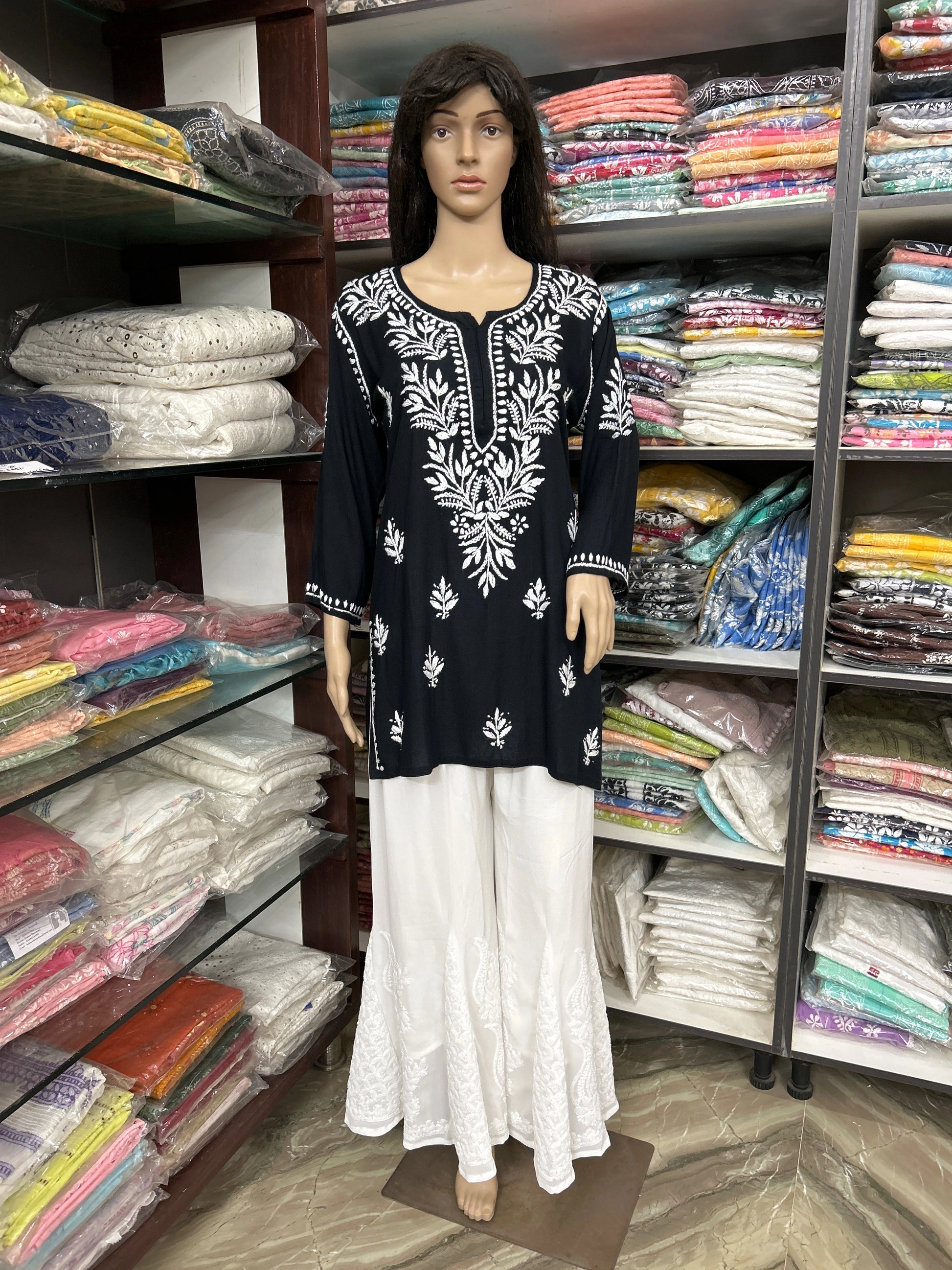 Mannequin wearing a black and white embroidered top with white pants in a fabric store.