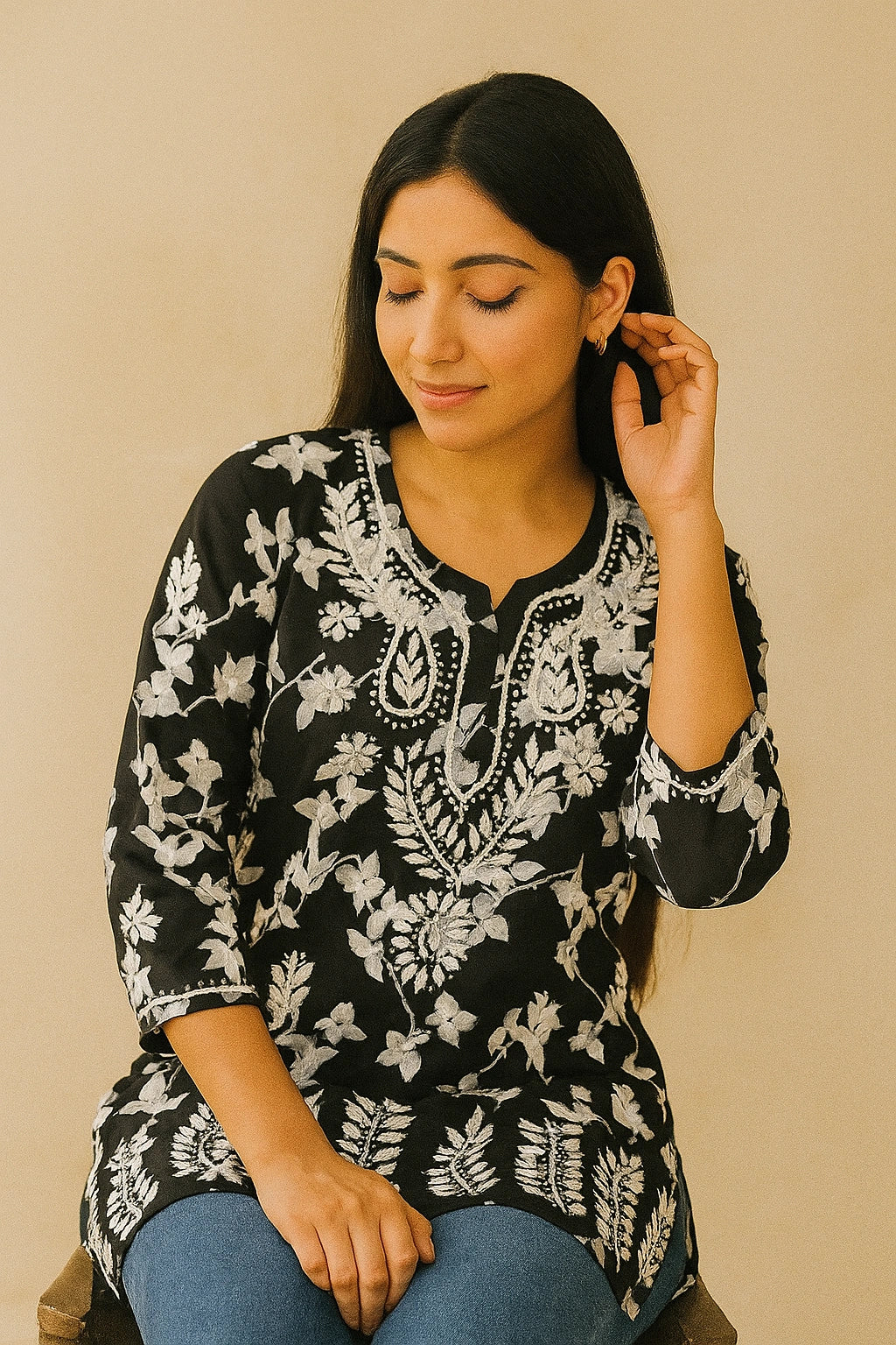 Woman wearing a black and white floral embroidered top against a beige background