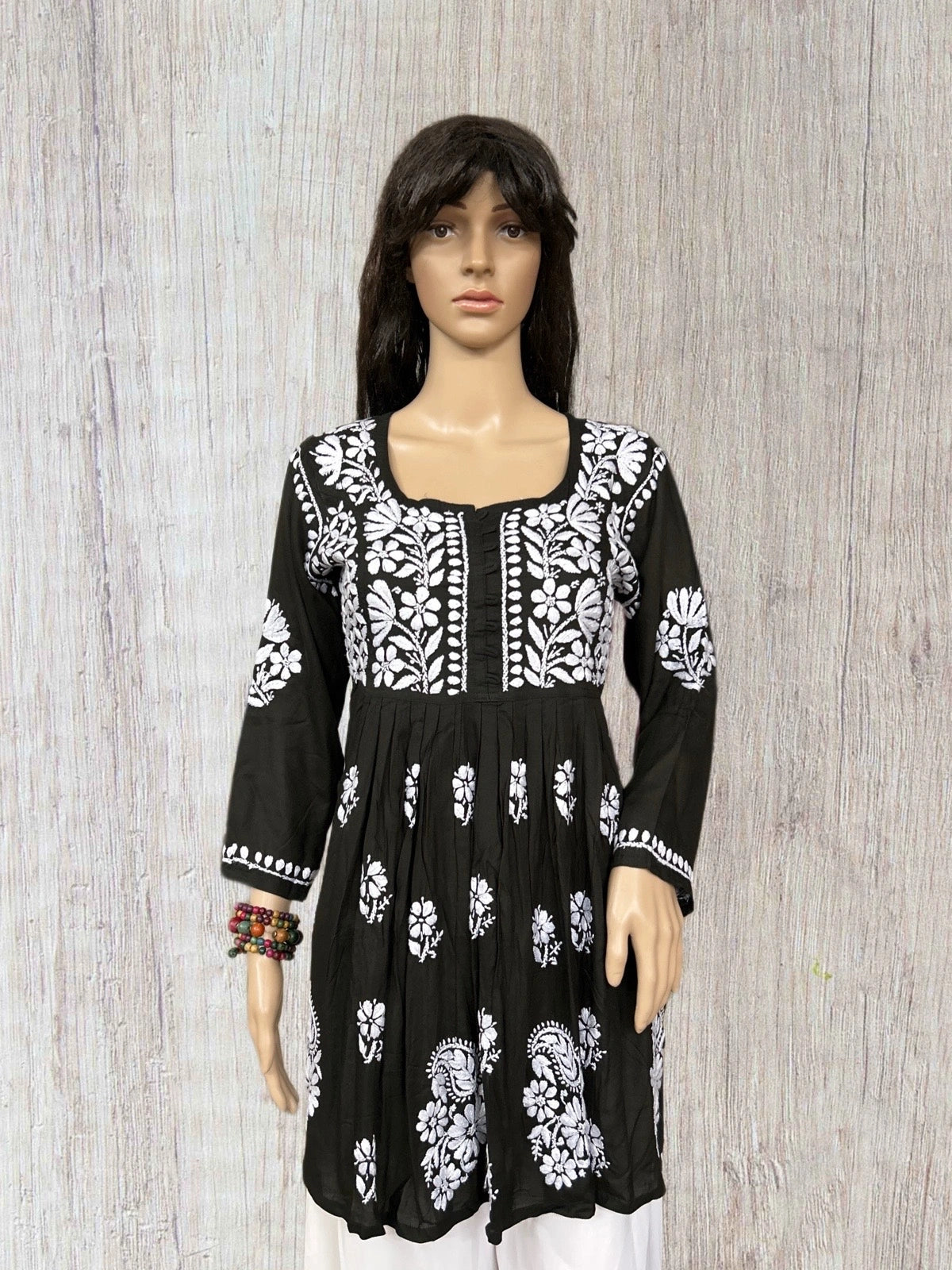 lucknowi chikankari Black dress with white floral patterns on a mannequin against a wooden background