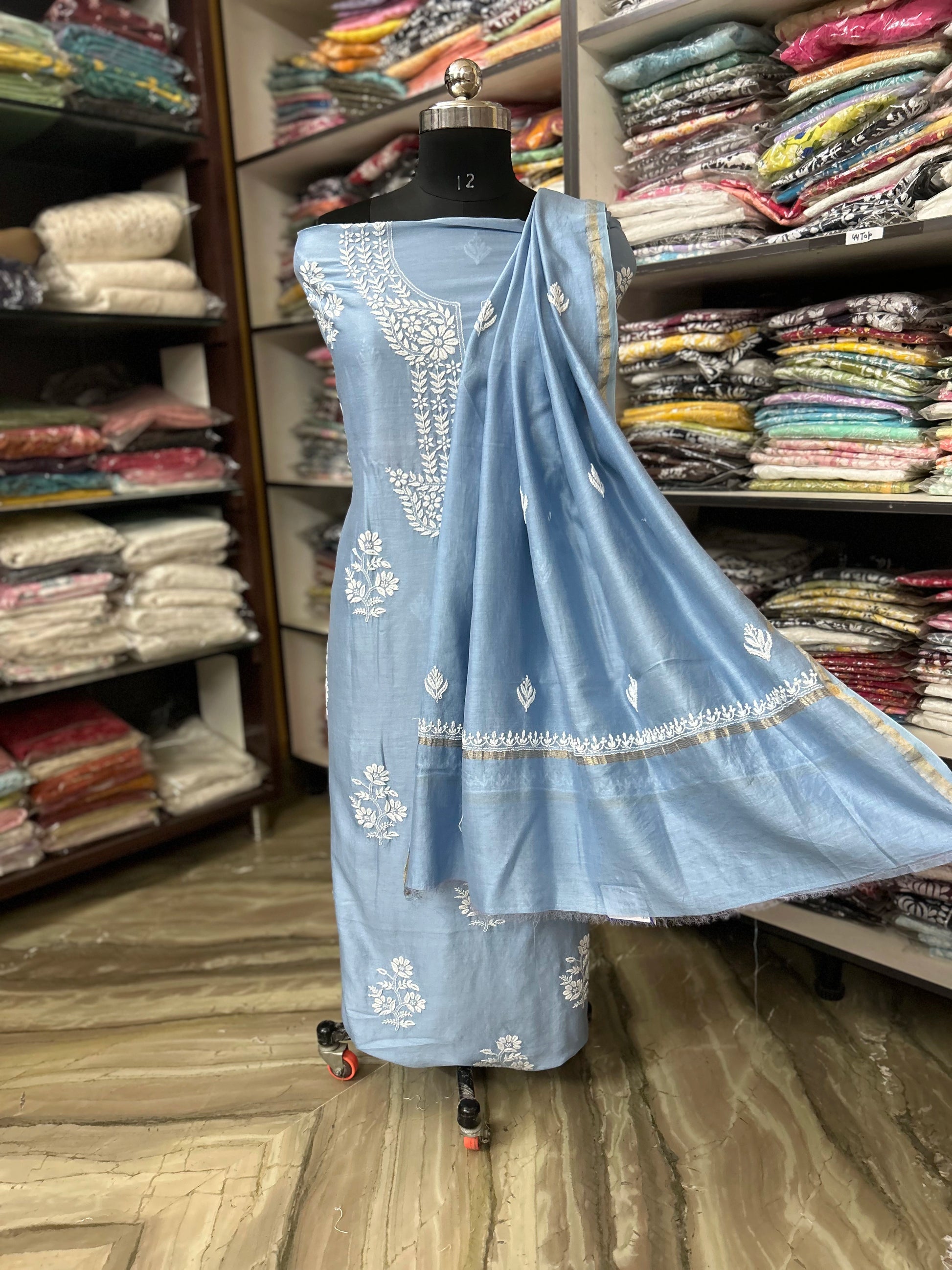 Light blue embroidered saree on a mannequin in a fabric store.