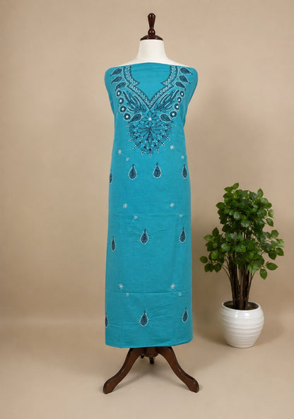 Turquoise embroidered dress on a mannequin with a plant in the background