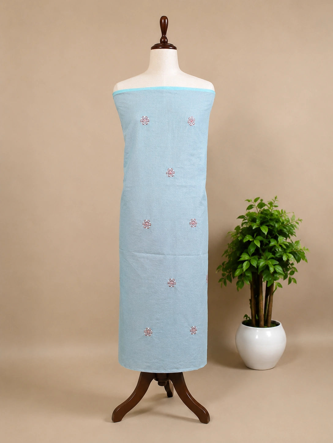 Lucknowi Chikankari Light blue fabric with red patterns on a mannequin against a beige background with a plant.