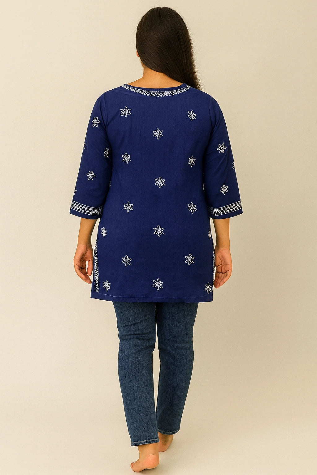 Woman wearing a blue embroidered top and jeans on a beige background