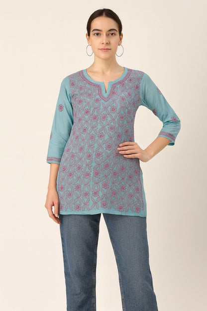 Woman wearing a lucknowi chikankari  light blue patterned top and jeans on a beige background