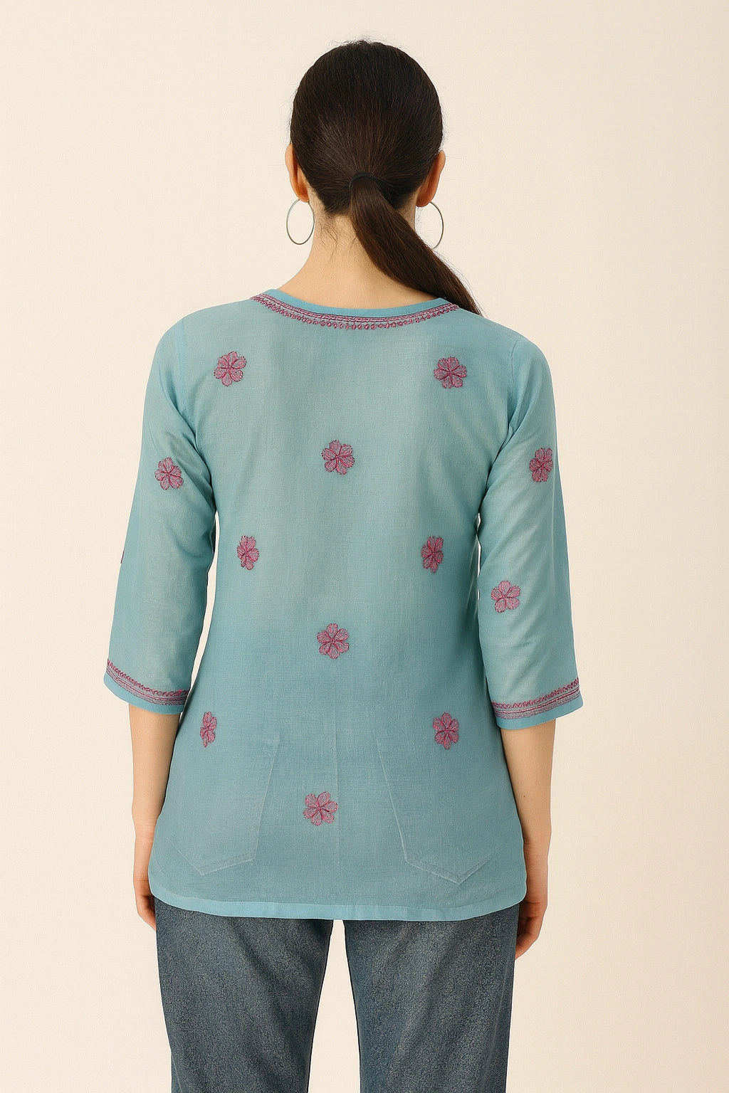 Woman wearing a light blue embroidered top on a beige background