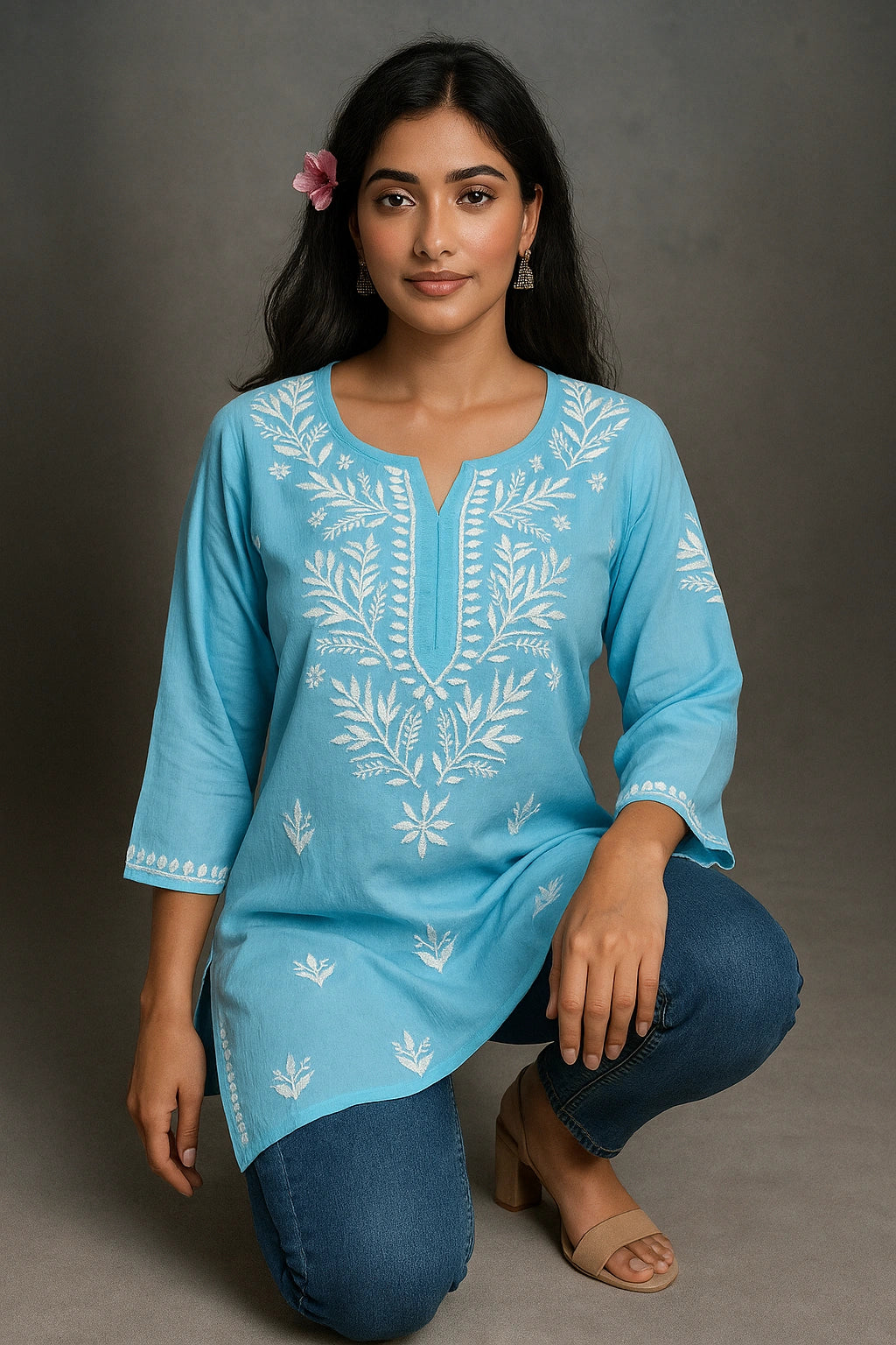Woman wearing a blue embroidered top and jeans on a gray background