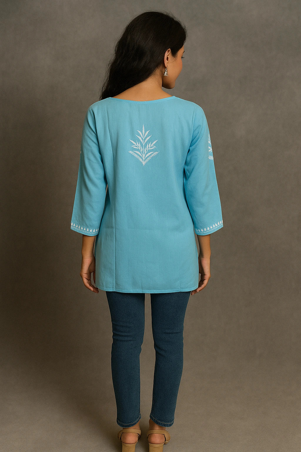 Woman wearing a light blue embroidered top and dark blue pants against a gray background